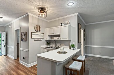 Kitchen with a sink, a textured ceiling, a breakfast bar area, white cabinetry, and light countertops