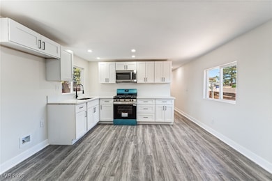 Kitchen with appliances with stainless steel finishes, white cabinets, dark wood-type flooring, and recessed lighting