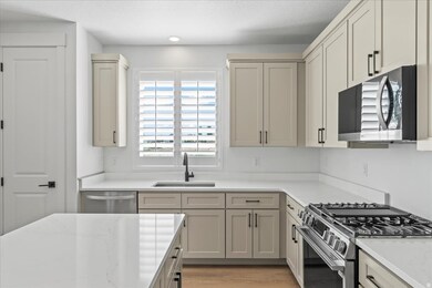 Kitchen featuring stainless steel appliances, light stone countertops, cream cabinetry, and light wood-type flooring