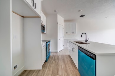 Kitchen with dishwasher, light wood finished floors, electric range, white cabinets, and a textured ceiling