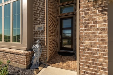 The entrance of a home showcase  a modern door framed by large windows, set against a brick exterior. A decorative statue adds charm to the entryway, and the well-maintained front area enhances curb appeal.