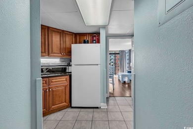 Kitchen featuring a textured wall, freestanding refrigerator, light tile patterned flooring, dark stone countertops, and a paneled ceiling