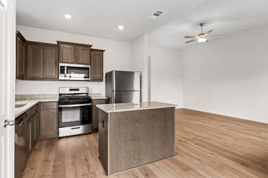 Kitchen with stainless steel appliances, dark brown cabinets, a center island, light stone countertops, and recessed lighting