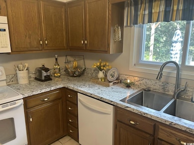 Kitchen with white appliances, brown cabinetry, and light stone countertops