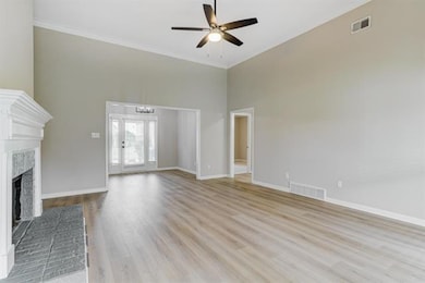 Unfurnished living room featuring light wood-style flooring, a towering ceiling, a brick fireplace, ceiling fan, and crown molding