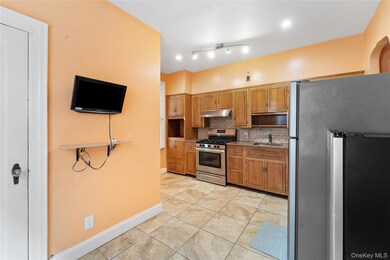 Kitchen with appliances with stainless steel finishes, backsplash, light tile patterned floors, light stone countertops, and brown cabinets