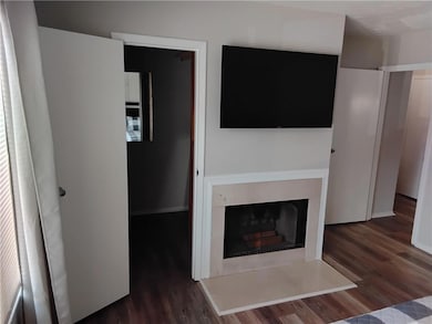 Unfurnished living room with dark wood-type flooring and a fireplace with raised hearth