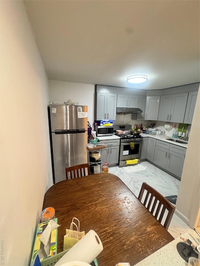 Kitchen featuring stove, fridge, light marble finish flooring, range hood, and gray cabinetry