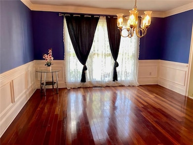 Empty room featuring a chandelier, a wainscoted wall, dark wood-style floors, ornamental molding, and a decorative wall