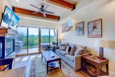 Living room featuring wood finished floors, recessed lighting, ceiling fan, a glass covered fireplace, and beamed ceiling