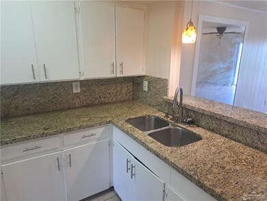 Kitchen featuring a ceiling fan, hanging light fixtures, light stone countertops, a sink, and white cabinetry