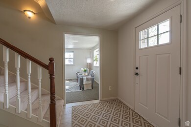 Entrance foyer with stairway, light tile patterned flooring, a textured ceiling, and baseboards