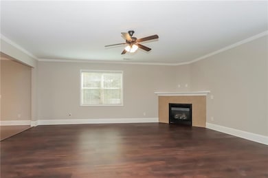 Unfurnished living room with wood finished floors, a tile fireplace, a ceiling fan, and ornamental molding