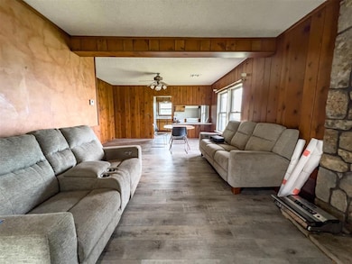 Living area with wood finished floors, wooden walls, a textured ceiling, and a ceiling fan
