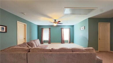 Carpeted living area with attic access and ceiling fan