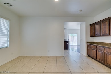 Kitchen with light tile patterned floors, dark brown cabinetry, and dark stone counters