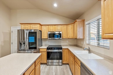 Kitchen with stainless steel appliances, lofted ceiling, light wood-style floors, recessed lighting, and light stone counters