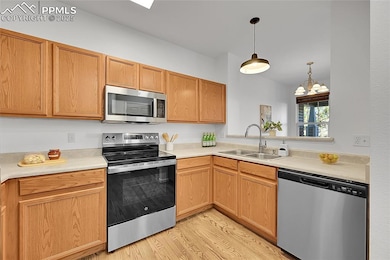 Kitchen with stainless steel appliances, light countertops, light wood finished floors, and pendant lighting