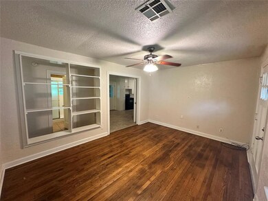 Empty room with wood finished floors, a textured ceiling, ceiling fan, baseboards, and built in shelves