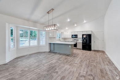 Kitchen featuring light countertops, black appliances, backsplash, light wood finished floors, and vaulted ceiling
