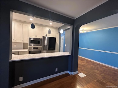 Kitchen with ornamental molding, white cabinetry, stainless steel appliances, and baseboards
