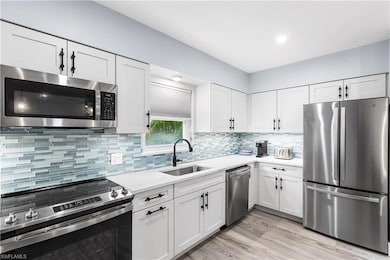 Kitchen featuring backsplash, white cabinets, appliances with stainless steel finishes, and a sink