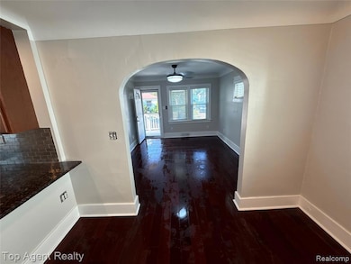 Unfurnished dining area featuring dark wood finished floors, arched walkways, and ceiling fan