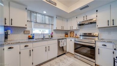 Kitchen with stainless steel appliances, white cabinets, light stone countertops, tasteful backsplash, and recessed lighting