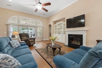 Living area with ceiling fan, crown molding, arched walkways, a glass covered fireplace, and a towering ceiling