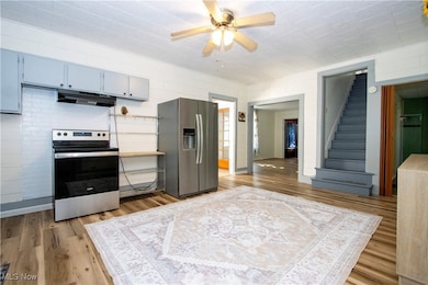 Kitchen with appliances with stainless steel finishes, gray cabinets, under cabinet range hood, light wood finished floors, and light countertops