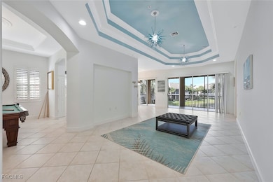 Living room featuring a tray ceiling, arched walkways, light tile patterned floors, and a chandelier