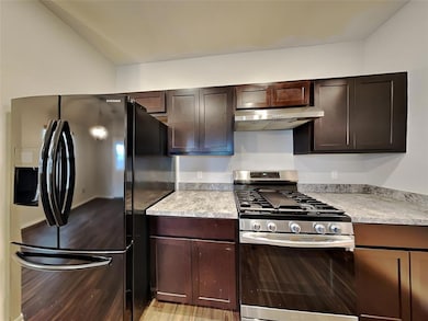 Kitchen featuring black fridge with ice dispenser, stainless steel range with gas cooktop, under cabinet range hood, dark brown cabinetry, and light countertops