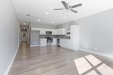 Kitchen featuring light hardwood / wood-style floors, white cabinets, backsplash, appliances with stainless steel finishes, and ceiling fan