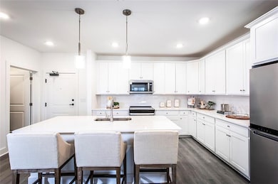 Kitchen with stainless steel appliances, a sink, dark wood-style flooring, a center island with sink, and light countertops