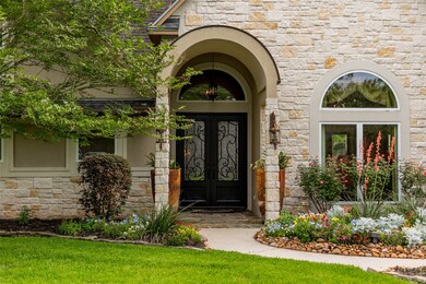Perfectly maintained flowerbeds full of colorful annuals with a rock-lined border line the path to a grand entrance with a barrel arch covered porch and a stately pair of solid metal double front doors with waterfall glass and scrolled iron detailing.
