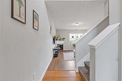 Hall with a textured ceiling, light wood-style floors, stairs, and baseboards