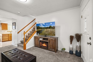 Living room with light colored carpet, a lit fireplace, stairway, and a textured ceiling