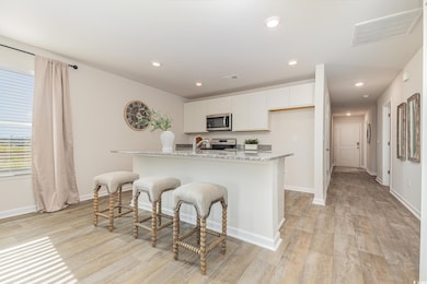 Kitchen featuring stainless steel appliances, light wood finished floors, white cabinetry, light stone countertops, and a kitchen bar