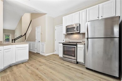Kitchen featuring stainless steel appliances, light wood-type flooring, white cabinetry, light countertops, and lofted ceiling