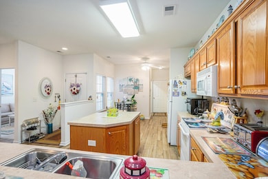 Kitchen with white appliances, light countertops, light wood-type flooring, a kitchen island, and recessed lighting