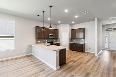 Kitchen featuring dark brown cabinets, a peninsula, decorative backsplash, light stone counters, and pendant lighting