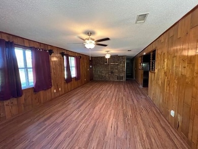 Spare room featuring a textured ceiling, ceiling fan, wood-type flooring, and wooden walls