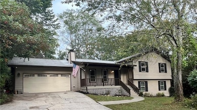 Split level home with a porch, concrete driveway, a chimney, a garage, and a front lawn