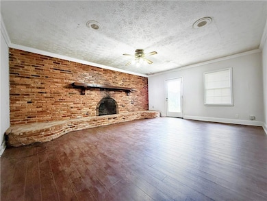Unfurnished living room with ceiling fan, a textured ceiling, dark wood finished floors, brick wall, and a fireplace