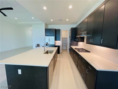 Kitchen featuring dark cabinetry, recessed lighting, backsplash, light stone counters, and an island with sink