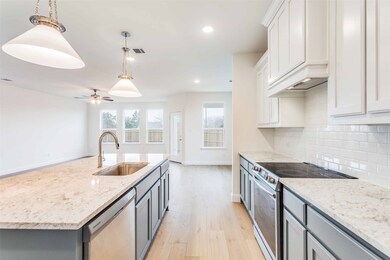 Kitchen featuring sink, white cabinetry, hanging light fixtures, stainless steel appliances, and a kitchen island with sink