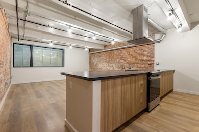 Kitchen featuring electric stove, island exhaust hood, brick wall, and light hardwood / wood-style floors
