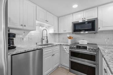 Kitchen with appliances with stainless steel finishes, white cabinets, tasteful backsplash, and light tile patterned floors