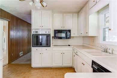 Kitchen with black appliances, wood walls, white cabinetry, brick patterned flooring, and ceiling fan