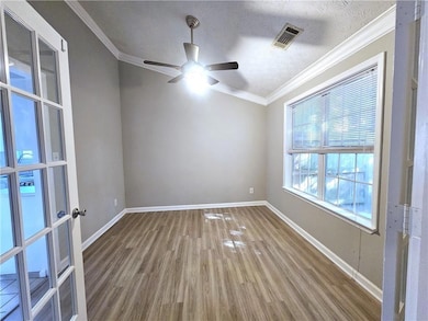 Empty room featuring wood finished floors, ceiling fan, ornamental molding, baseboards, and a textured ceiling